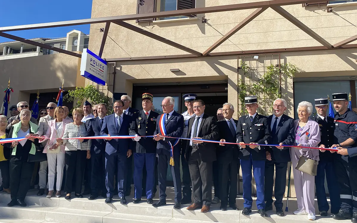 Un groupe de personnes participe à une cérémonie d'inauguration avec découpe de ruban devant un bâtiment de police municipale.
