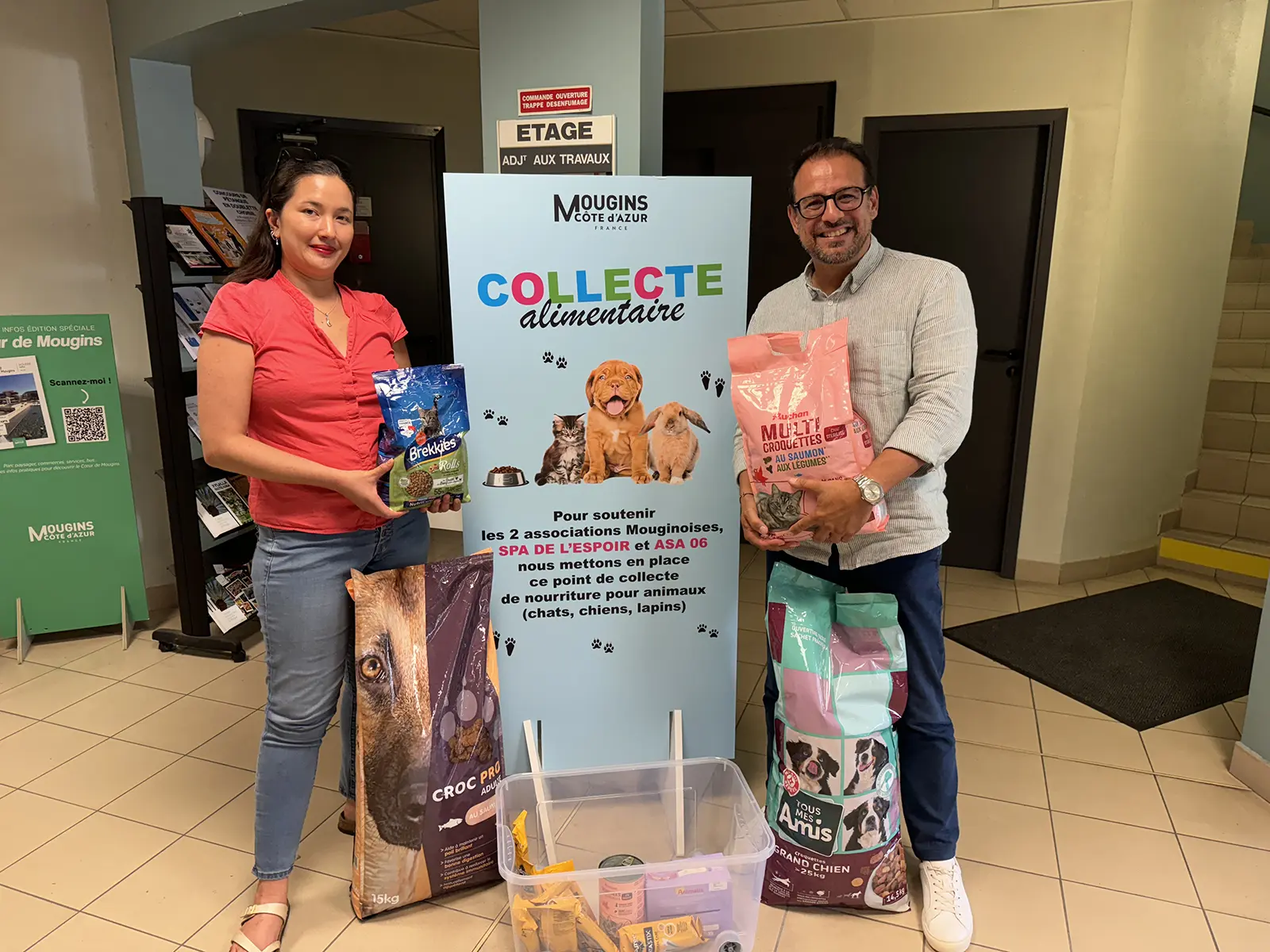 Deux personnes dans un hall participent à une collecte alimentaire pour animaux à Mougins, Côte d'Azur, avec des sacs de nourriture pour animaux.