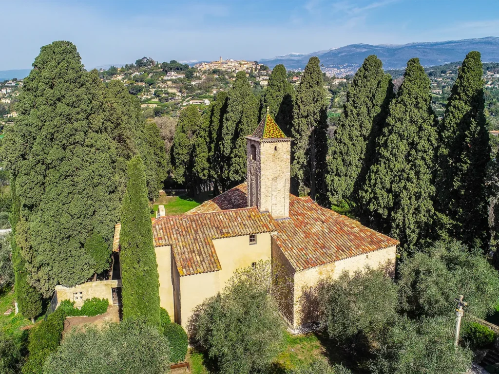 Promouvoir et préserver notre mémoire 6 Une ancienne chapelle entourée de grands arbres à Saint-Paul-de-Vence, offrant une vue panoramique sur le paysage provençal environnant.